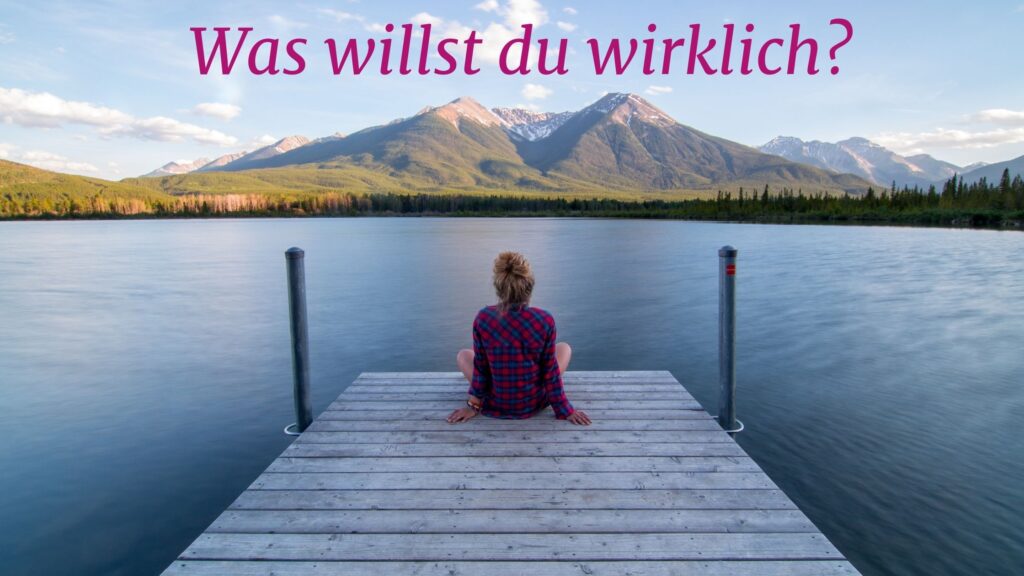 Frau am See mit Bergen im Hintergrund denkt über ihre Lebensaufgabe nach